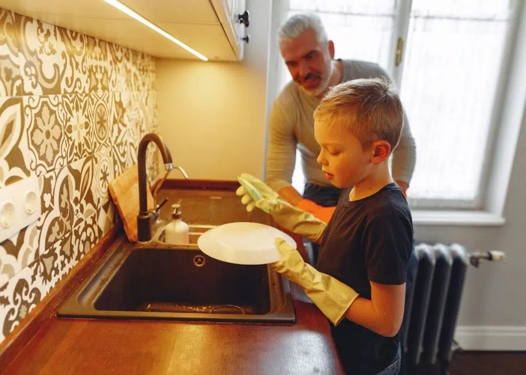 A father is teaching his son how to wash dishes as part of his daily chores.