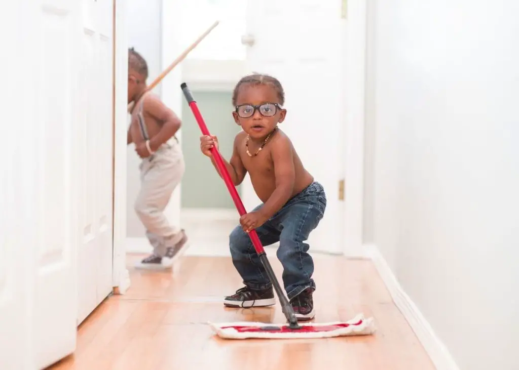 Two toddler boys are mopping the floor as part of their individual chores.