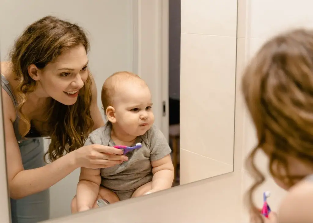 A mom is helping her baby brush his teeth with a toothbrush.