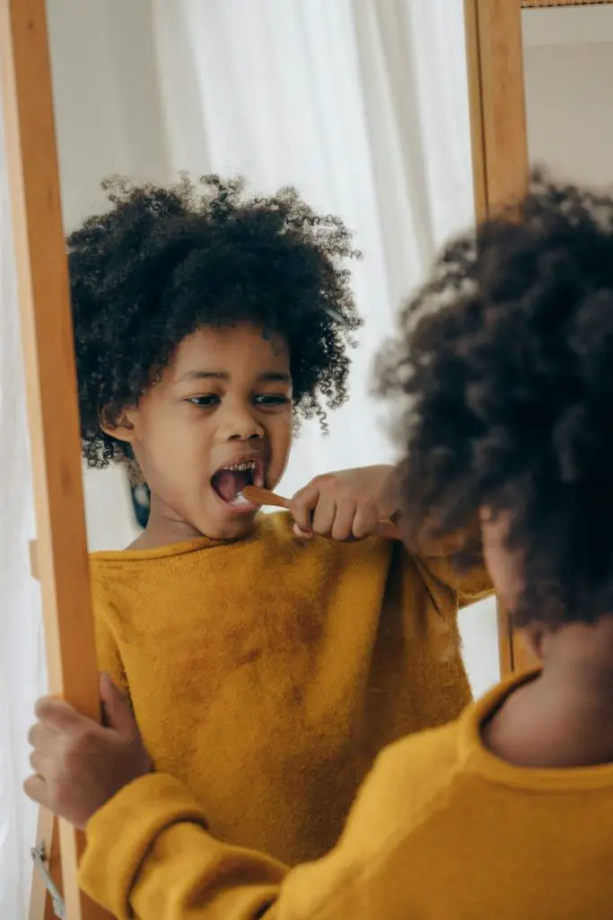 A toddler boy is looking in the mirror while he brushes his teeth.