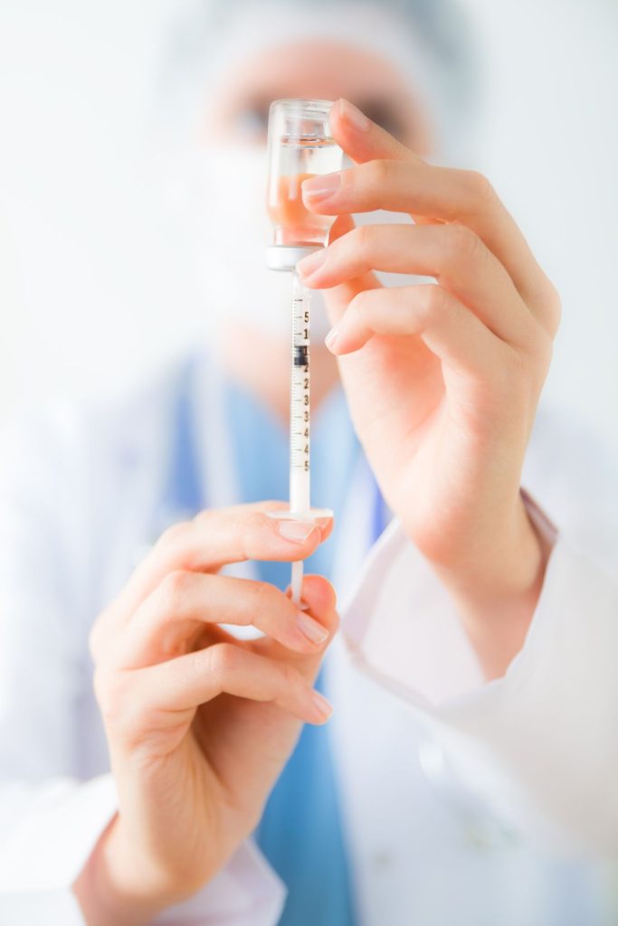 A closeup of a nurse is filling a syringe with a vaccine.