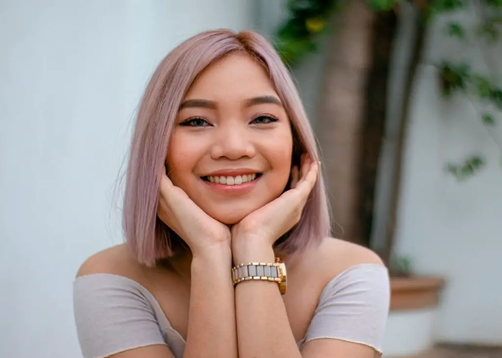 A teenage girl with lilac hair is smiling.