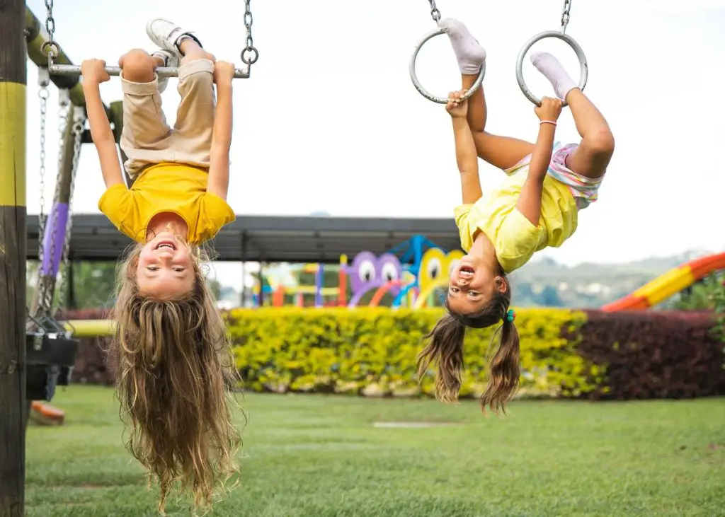 Two young girls wearing yellow shirts are playing on a play set.